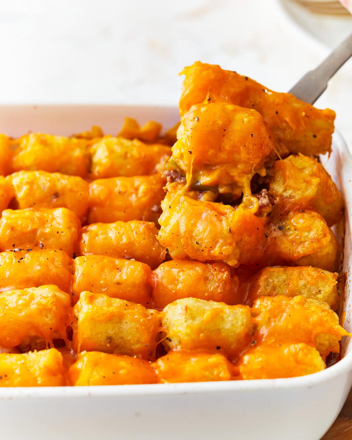 a spoon scooping a helping of sloppy joe tater tot casserole from a casserole dish.