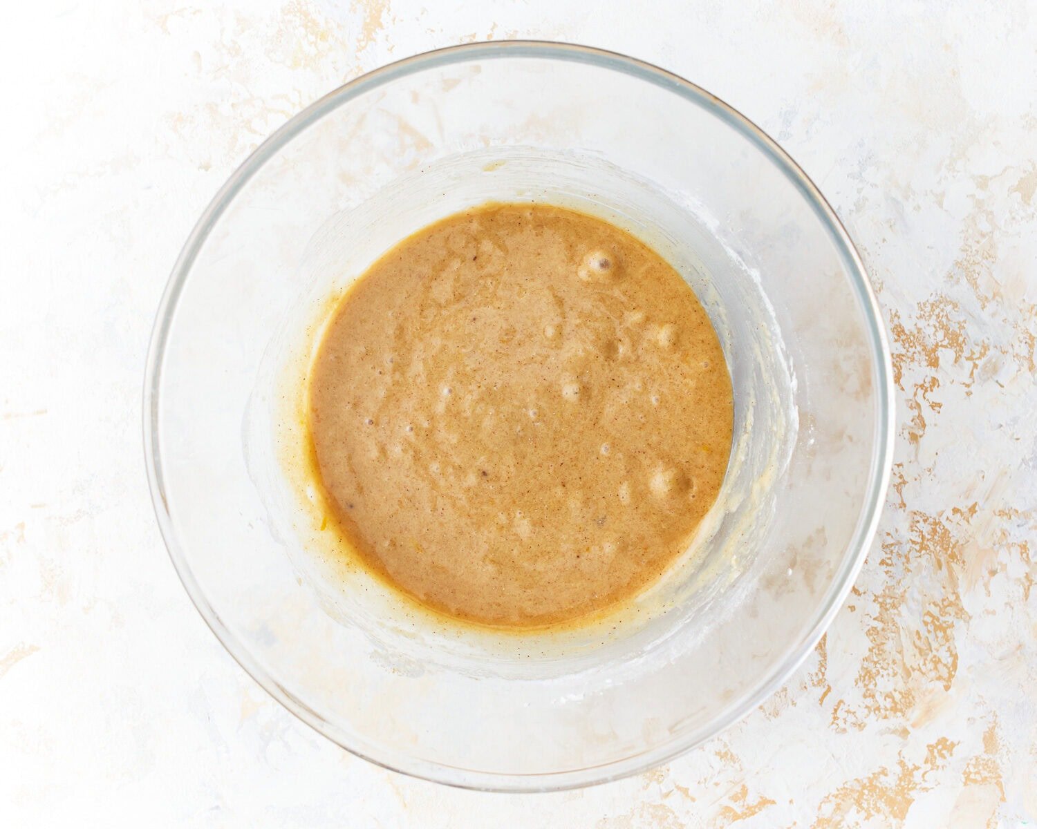 Gluten-free flour added to wet ingredients for gluten-free zucchini bread in a glass mixing bowl.