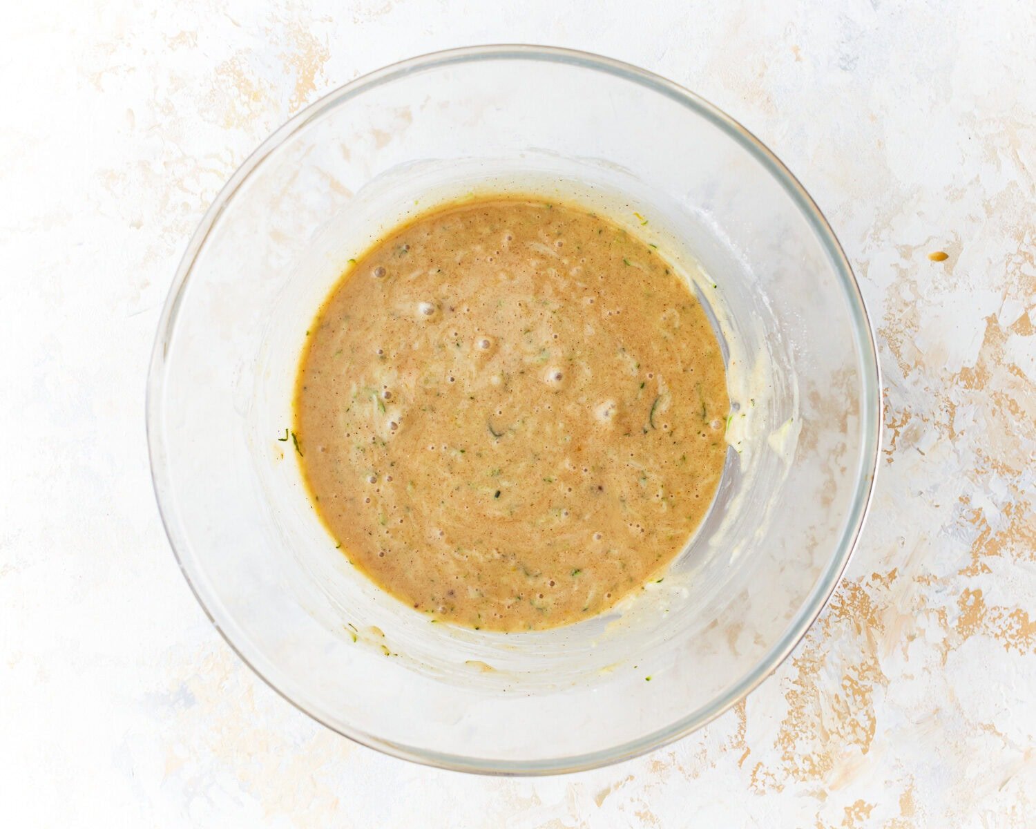 Wet ingredients for gluten-free zucchini with shredded zucchini added in a glass mixing bowl.