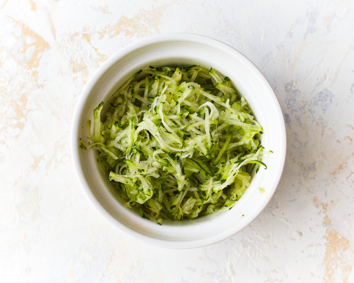 Grated zucchini in a glass mixing bowl.