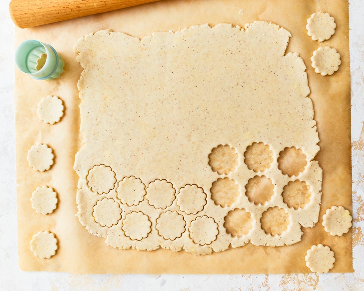 A cookie cutter cutting out ritz cracker shapes from rolled out gluten-free dough on parchment paper.