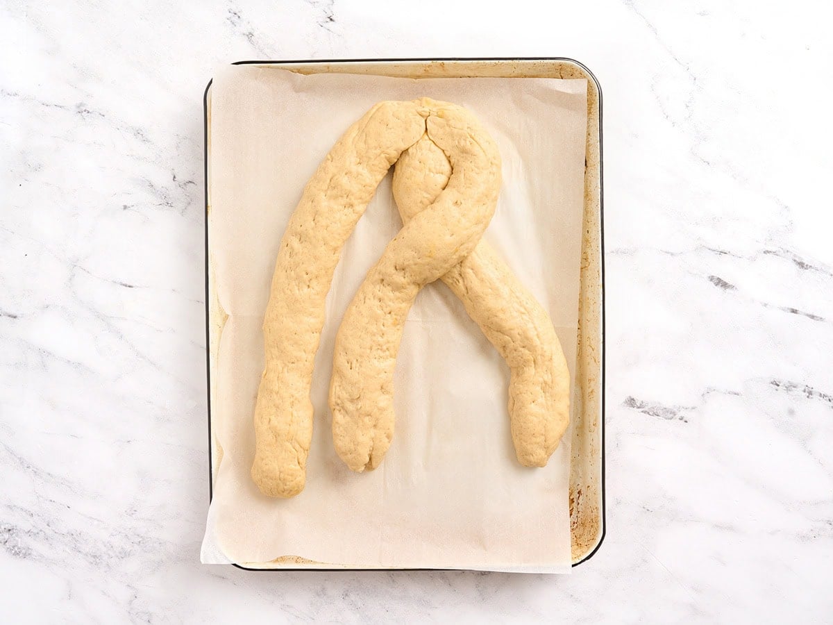 Three ropes of gluten free challah bread dough arranged on a parchment lined baking sheet to begin braiding.