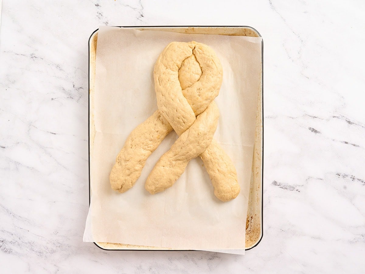 Right strand of gluten free challah bread dough crossed over the center strand while braiding.