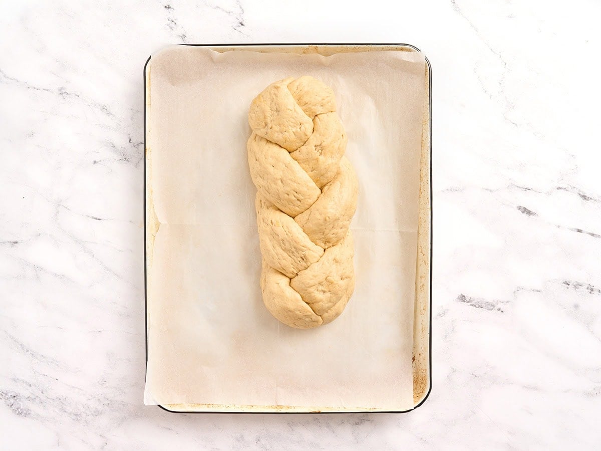 Fully braided gluten free challah bread dough shaped on a parchment lined baking sheet.