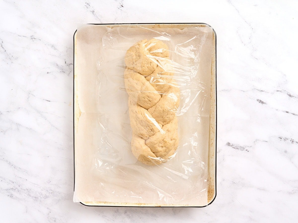 Braided gluten free challah bread dough loosely covered with plastic wrap for the second rise.