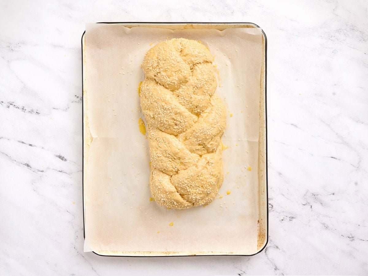 Braided gluten free challah bread brushed with egg wash and topped with sesame seeds before baking.