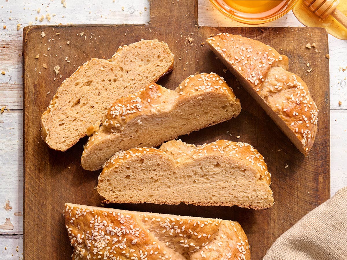 Sliced gluten free challah bread with sesame seeds showing the soft interior crumb on a wooden board.