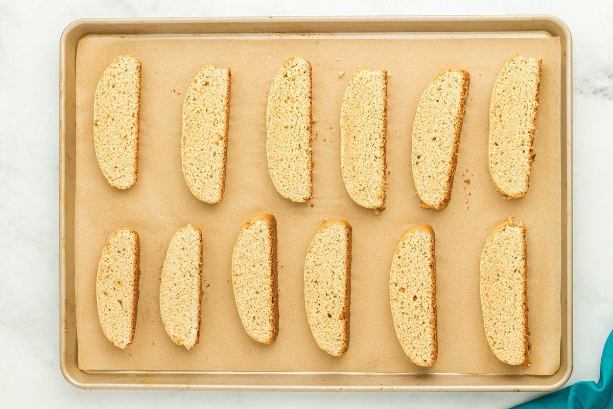 a bunch of sliced biscotti lined up on a lined baking sheet