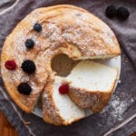 gluten-free angel food cake sliced on a grey towel sprinkled with powdered sugar and a few berries.