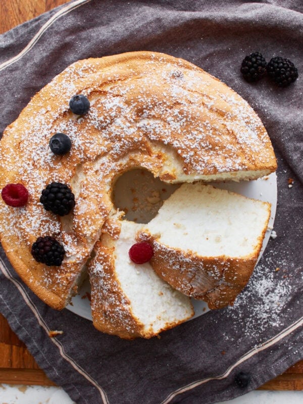 gluten-free angel food cake sliced on a grey towel sprinkled with powdered sugar and a few berries.
