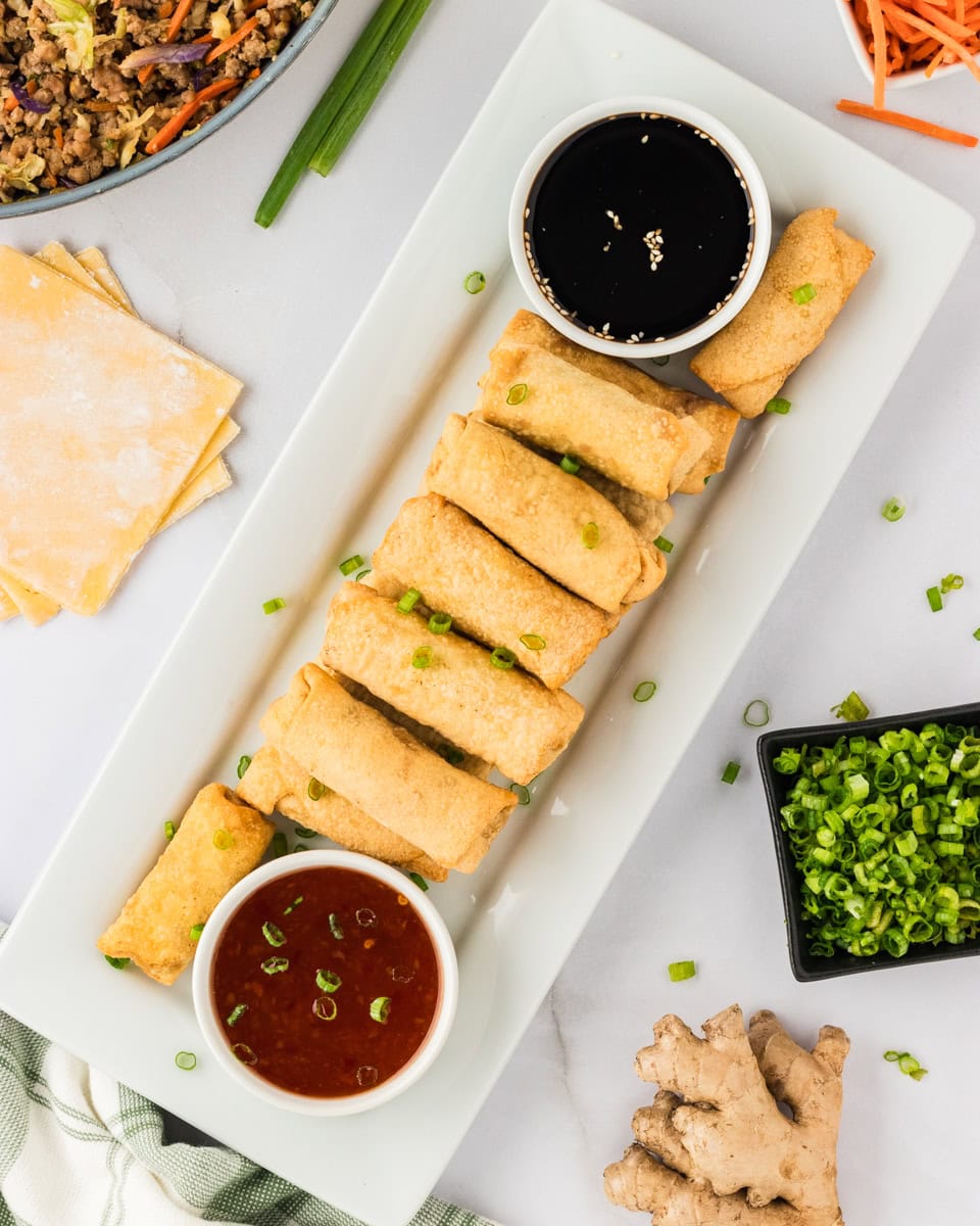 a bunch of gluten-free egg rolls on a white rectangular plate with sweet chili sauce and soy sauce