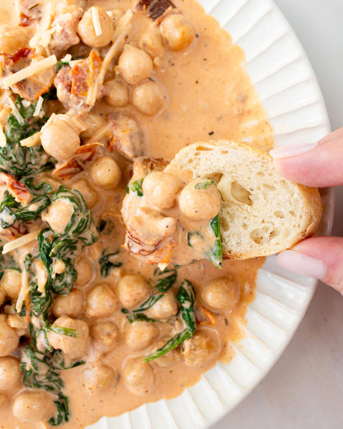 hand dipping a piece of bread into marry me chickpeas in white bowl