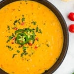 closeup of vegan queso in a black skillet topped with jalapenos and red peppers