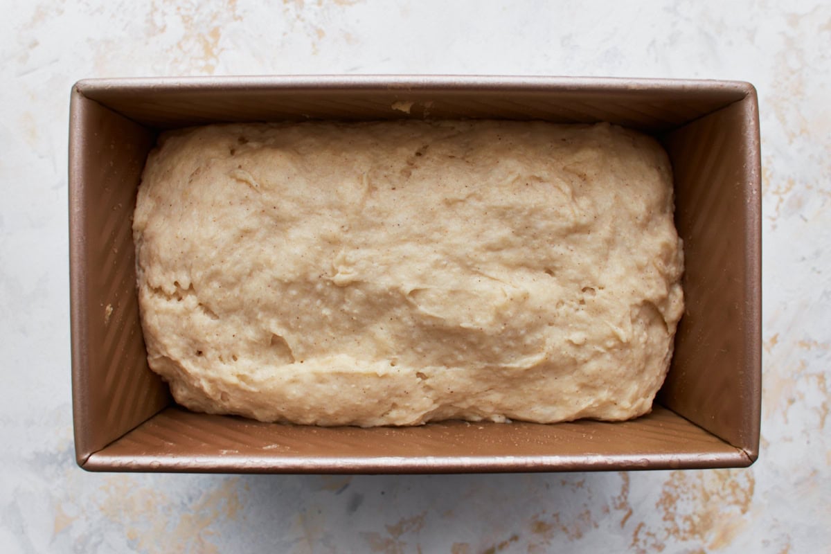 gluten-free bread dough in bread pan, risen and proofed on a white counter top.