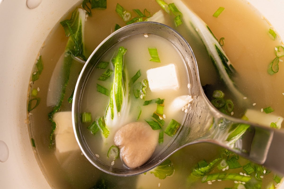 stainless steel ladle scooping gluten-free miso soup out of large pot 