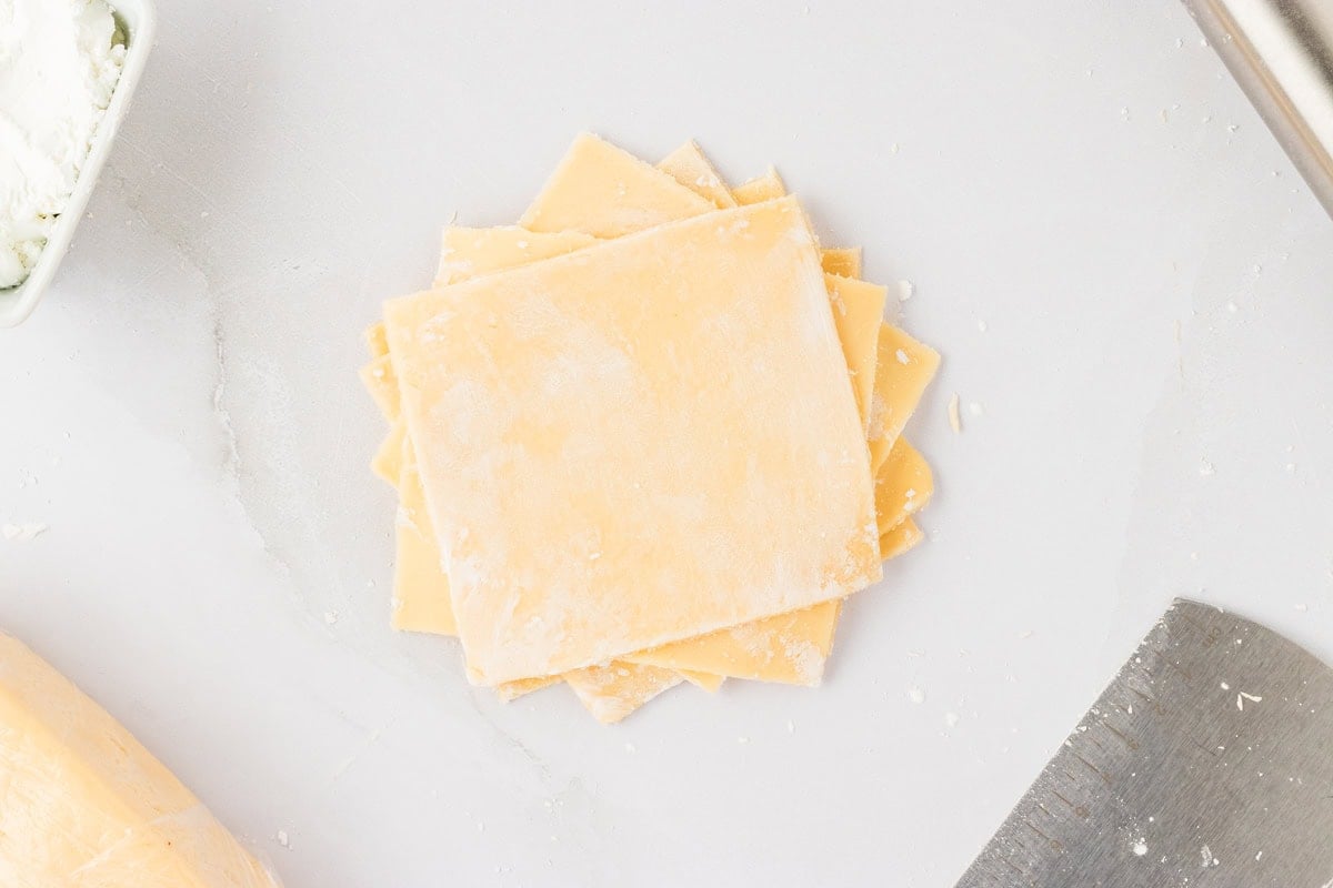 a lot of 4-inch squares of gluten-free egg roll dough stacked on top of each other and dusted with cornstarch