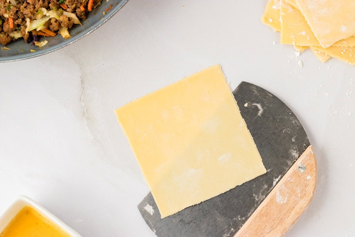 1 square of gluten-free egg roll dough being picked up by dough cutter