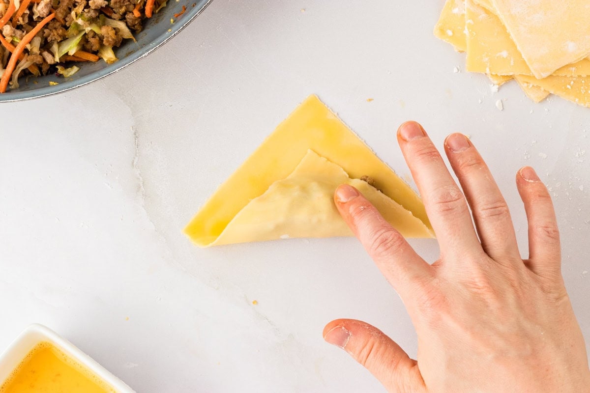 corner of gluten-free egg roll dough square being folded over filling 