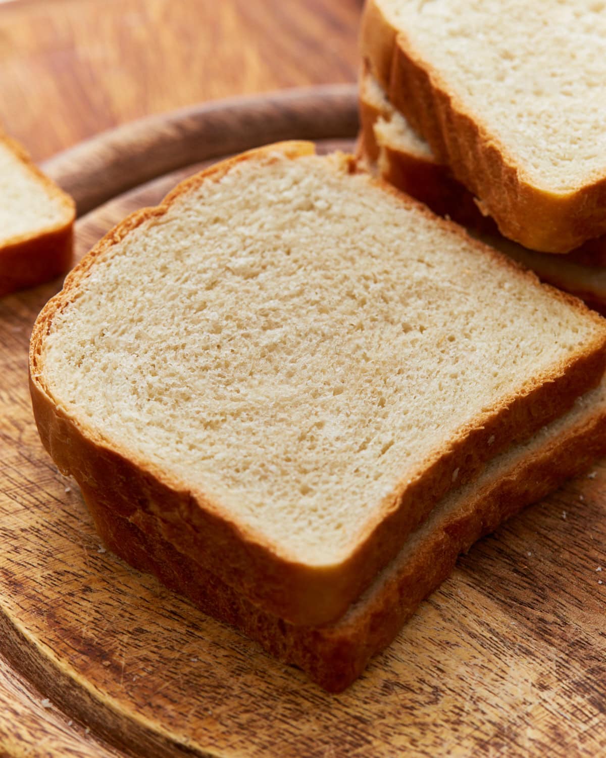 Two pieces of gluten-free bread stacked on top of a circular wooden cutting board with other pieces of gluten-free bread in the background.