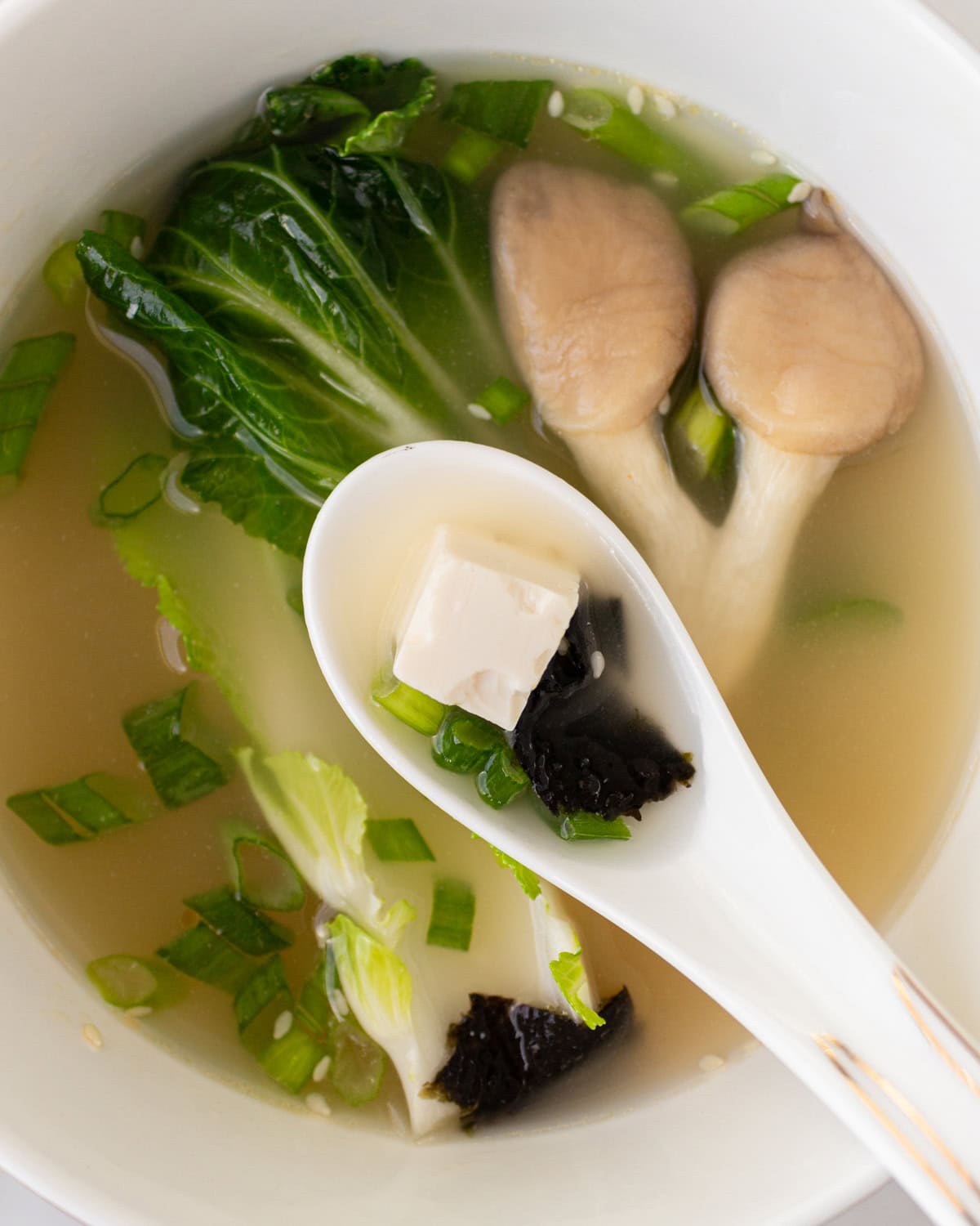 white soup spoon with a piece of tofu and seaweed hovering over bowl of gluten-free miso soup