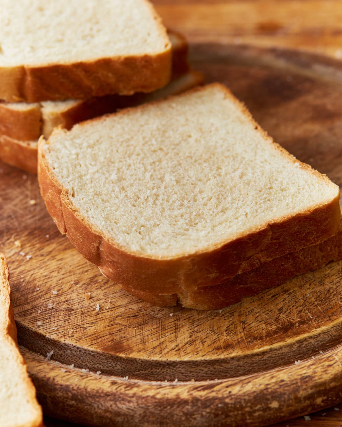 Two pieces of gluten-free bread stacked on top of a circular wooden cutting board with three pieces of gluten-free bread stacked in the background.