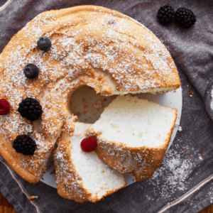 gluten-free angel food cake sliced on a grey towel sprinkled with powdered sugar and a few berries.