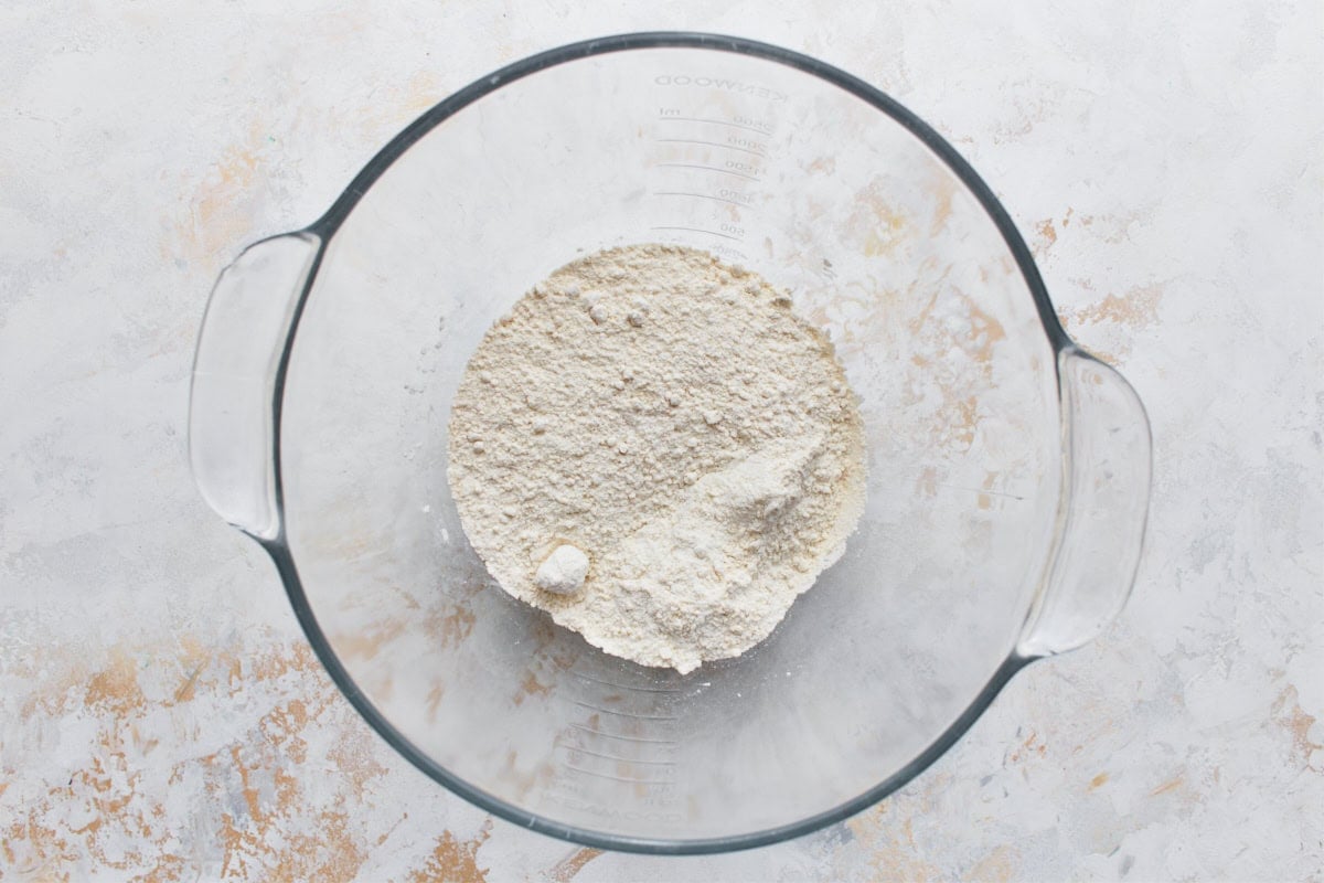 Gluten-free flour, baking powder, and instant yeast mixture in glass bowl.