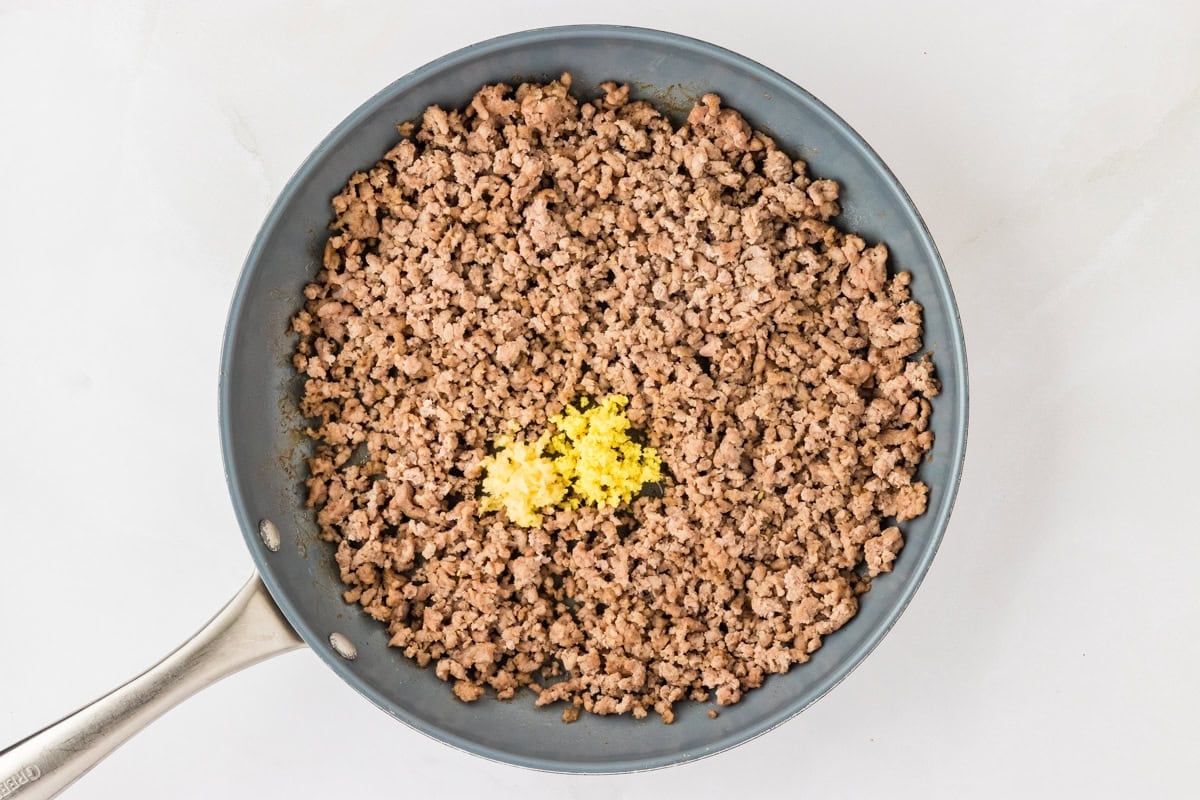 ground pork in skillet with minced ginger and minced garlic on top