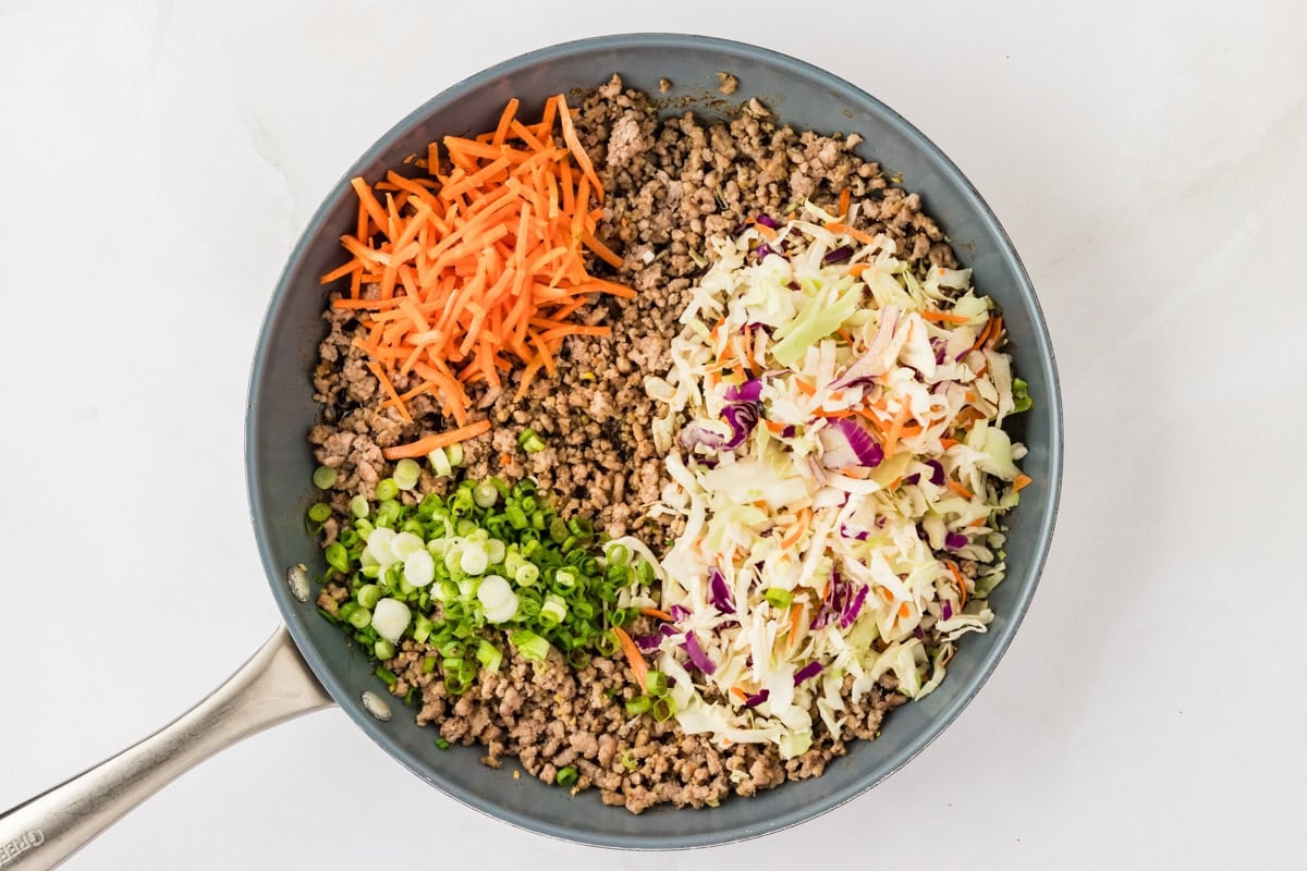 ground pork in a skillet with coleslaw mix, carrots, and green onion on top