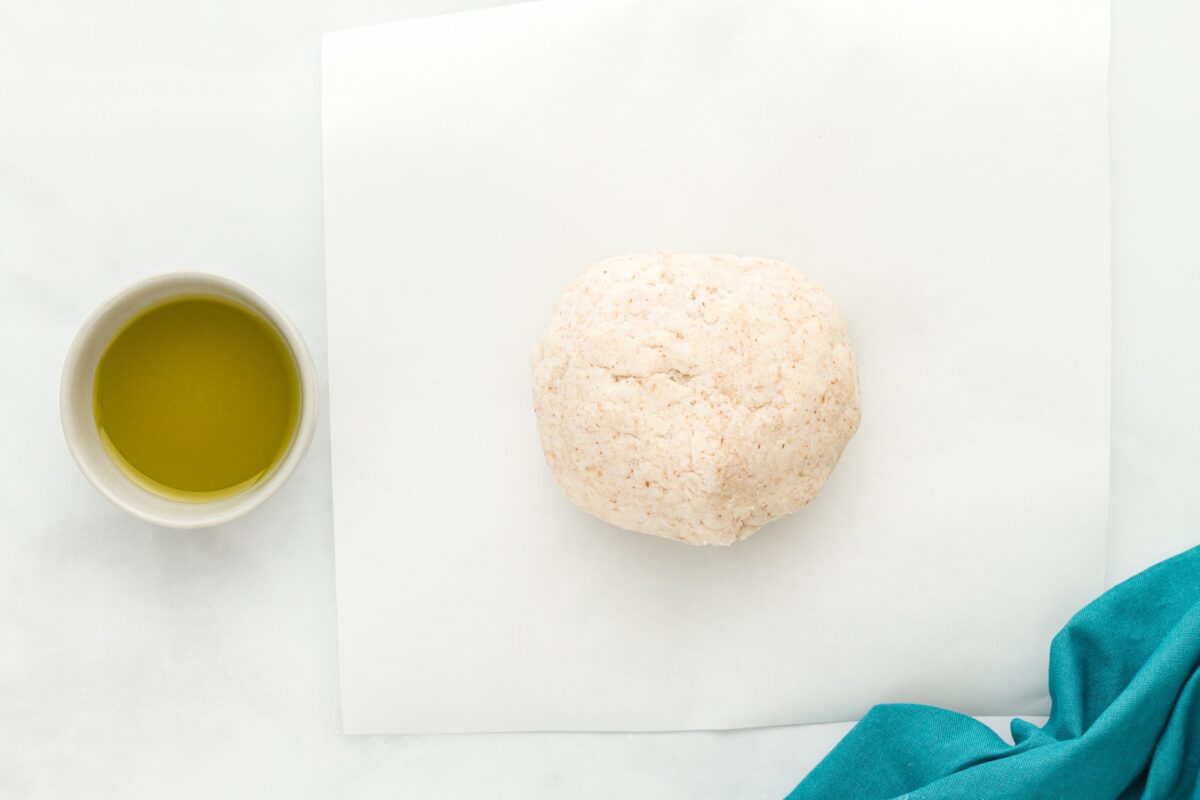 a ball of coconut flour dough in a piece of parchment paper next to a small bowl with olive oil