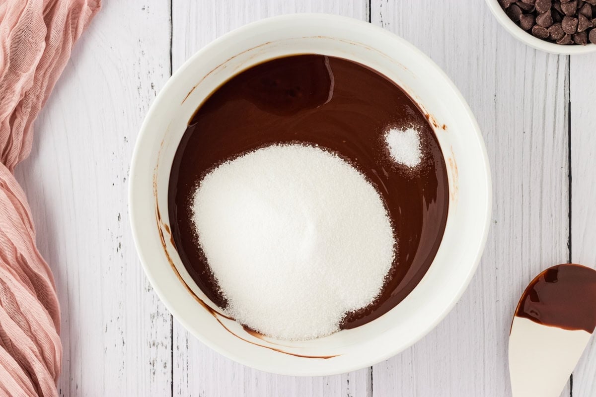 melted chocolate in a white bowl with white sugar, salt, and vanilla extract