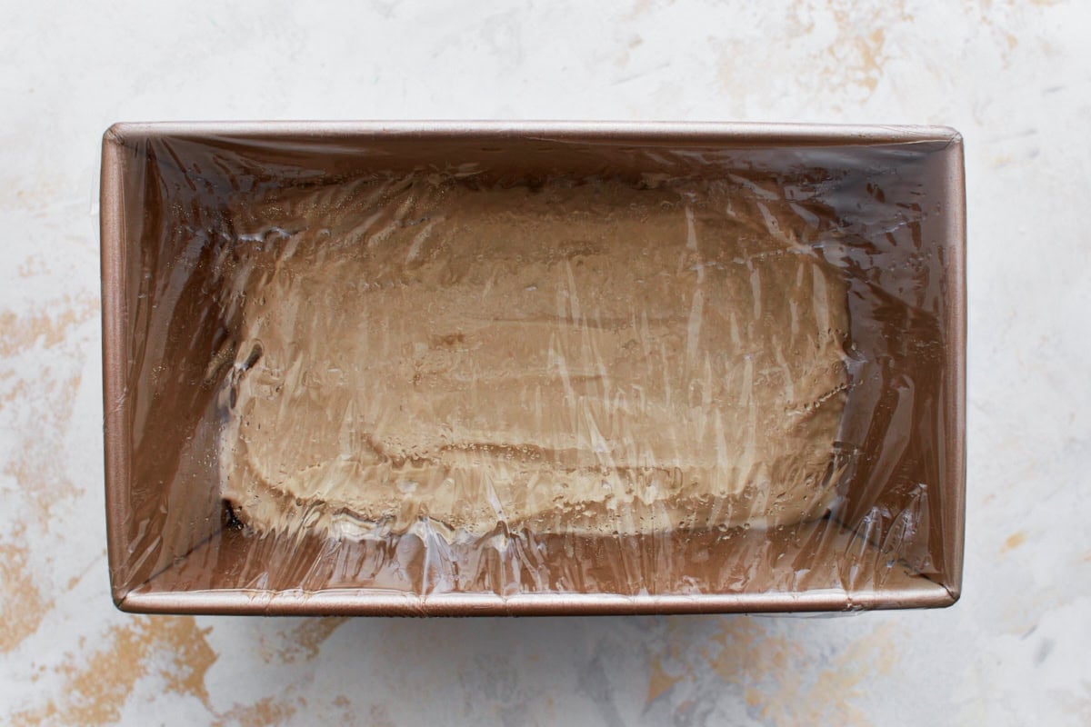 gluten-free bread dough in bread pan with plastic wrap covering it on a white counter top