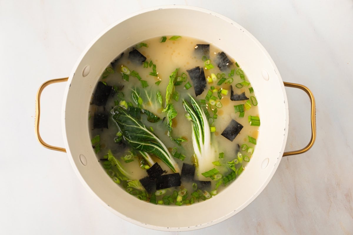 gluten-free miso soup cooking in a large pot with baby bok choy, green onions, and seaweed floating