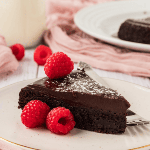 piece of flourless chocolate cake on a white plate topped with powdered sugar and raspberries