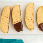 2 plain and 2 chocolate dipped biscotti on a white serving platter with a cup of melted chocolate