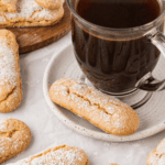 black coffee in a clear mug, on a white saucer with a ladyfinger on it