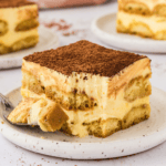 piece of tiramisu on white plate with more plates in the background