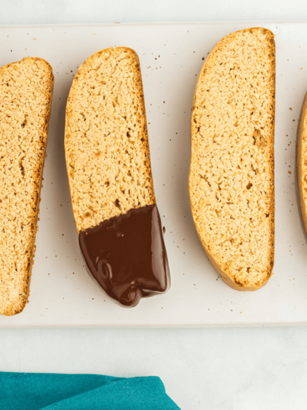 2 plain and 2 chocolate dipped biscotti on a white serving platter with a cup of melted chocolate