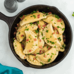 over head view of pierogis in cast iron pan with bacon, scallions on a white counter