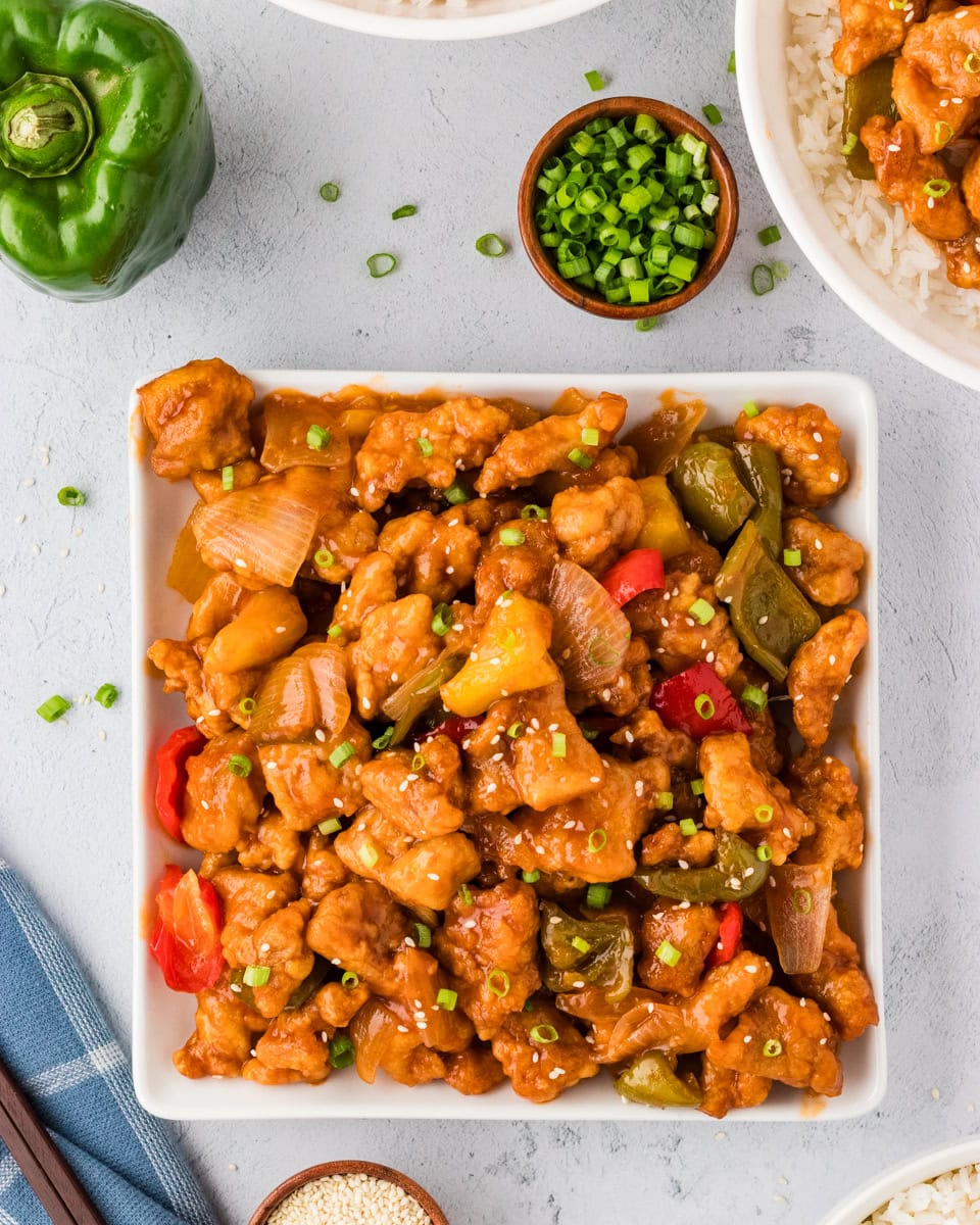overhead view of sweet and sour chicken with veggies in square white bowl