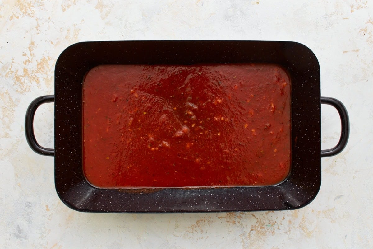 black baking dish with marinara sauce spread on the bottom