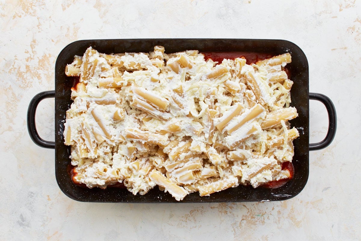black baking dish with cheese covered gluten-free pasta on top of a layer of marinara sauce
