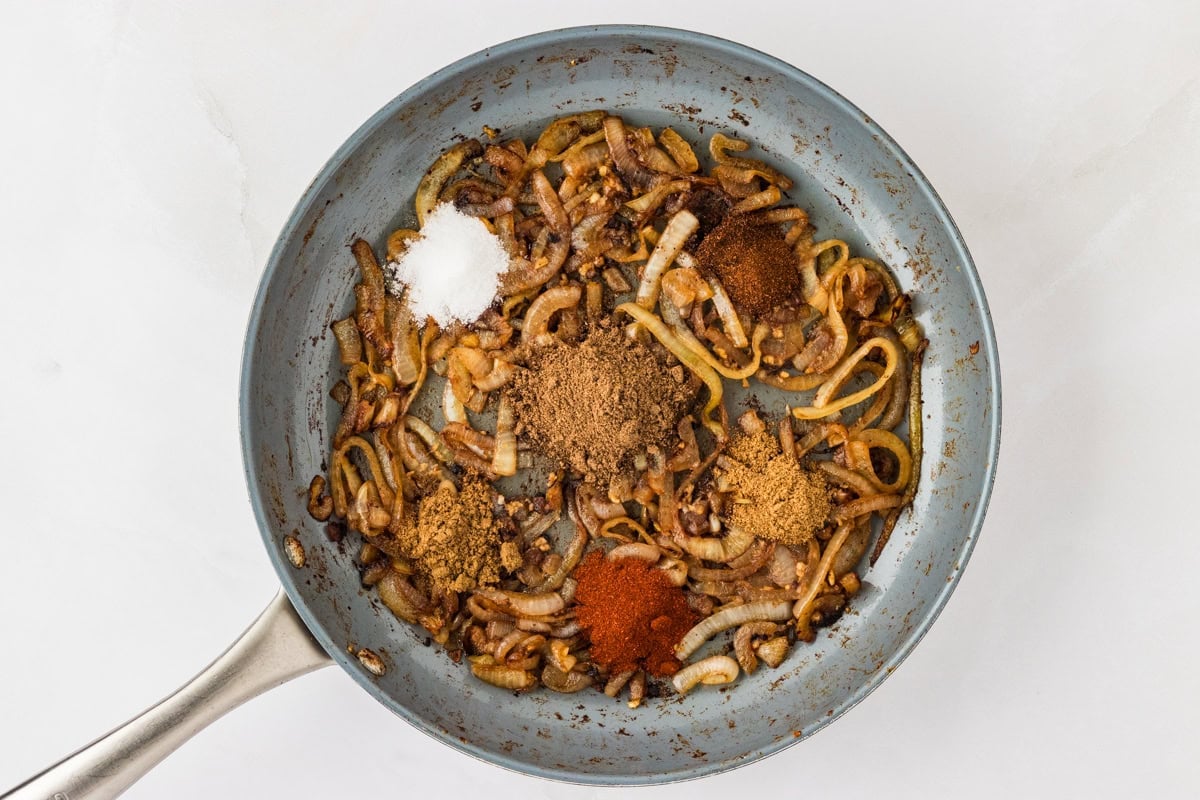 garam masala, cumin, chili powder, paprika, and salt on sautéed onions in a skillet