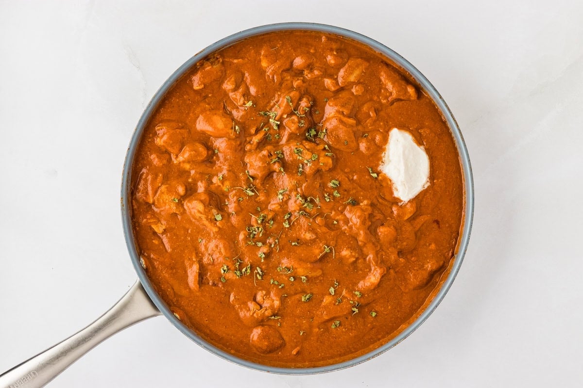 dairy-free butter chicken sauce in a skillet with chicken mixed in and a dollop of vegan butter