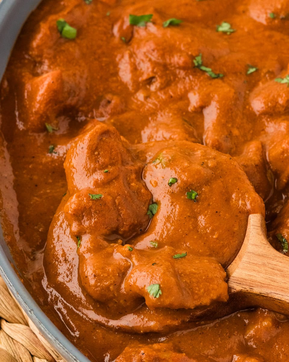 zoomed in picture of butter chicken in a skillet with wooden spoon