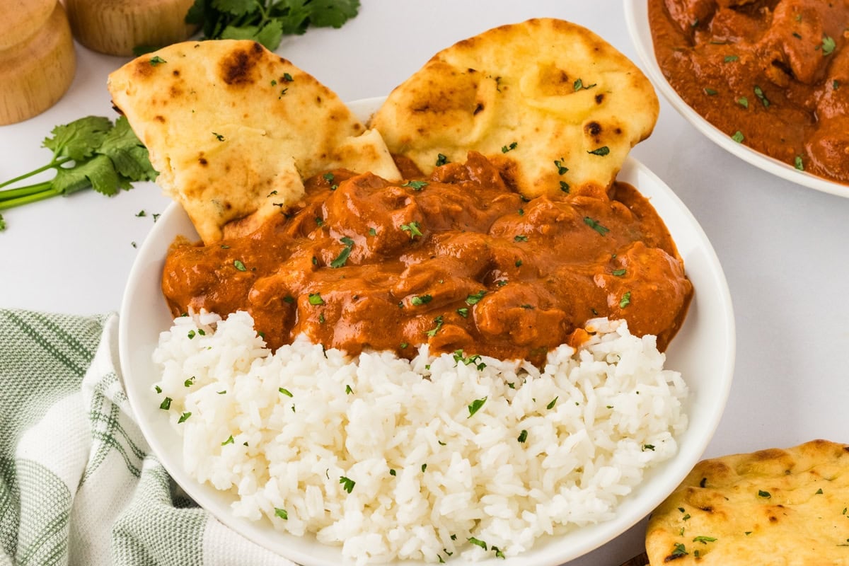 dairy free butter chicken over basmati rice in a white bowl with naan bread