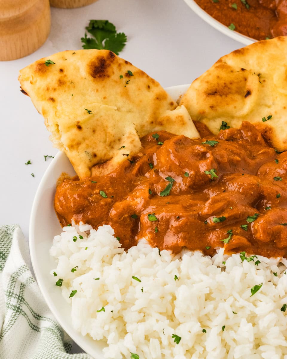 dairy free butter chicken over basmati rice in a white bowl with naan bread