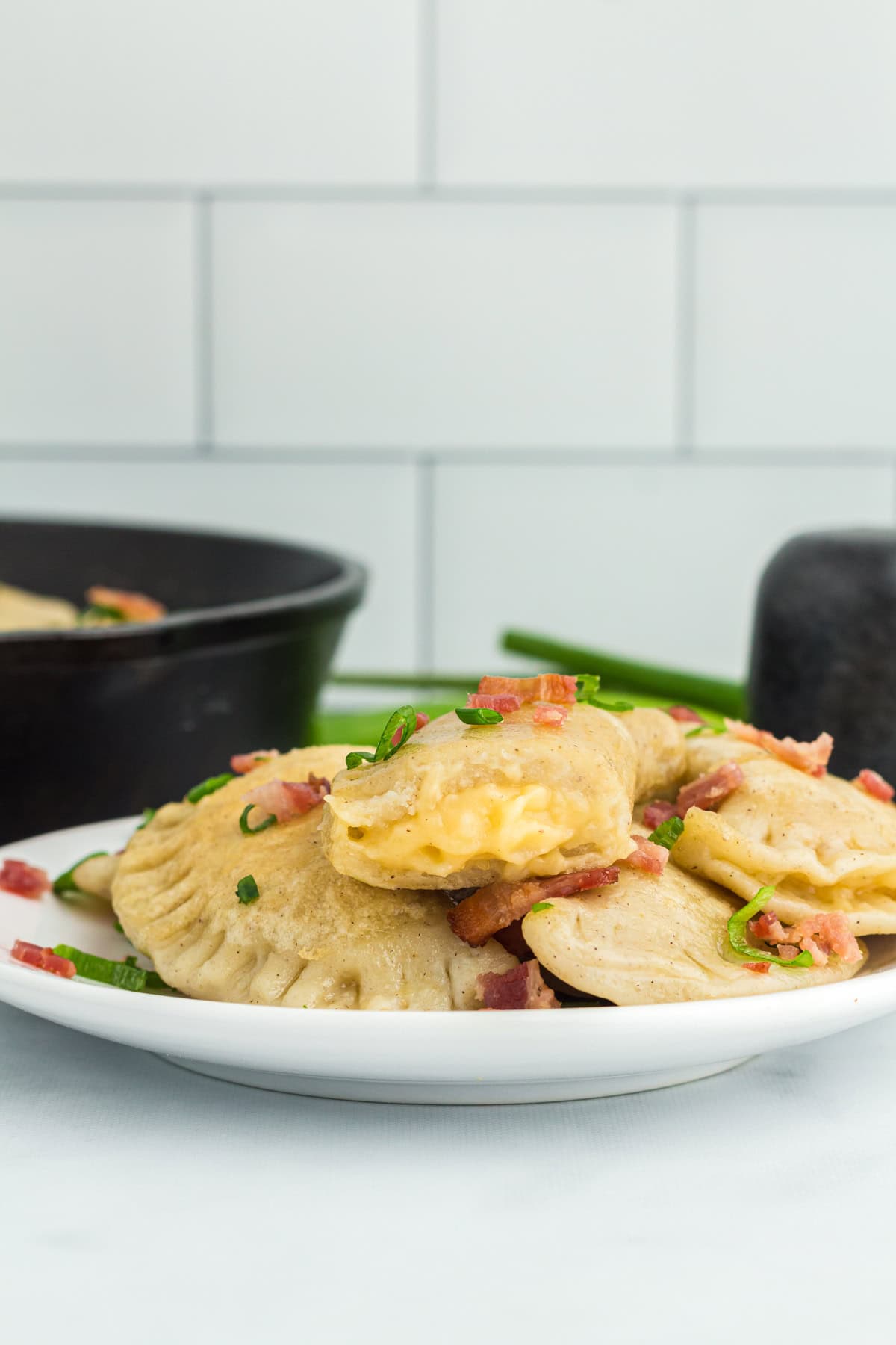 side view of pierogi on white plate with cast iron pan in the background