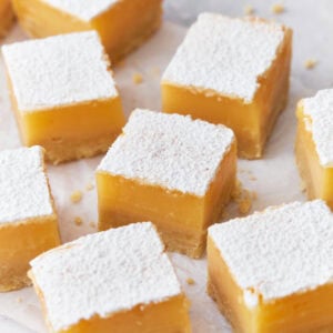 Close-up of gluten-free lemon bars, featuring a thick, vibrant yellow lemon filling on a shortbread crust, dusted generously with powdered sugar, arranged neatly on parchment paper