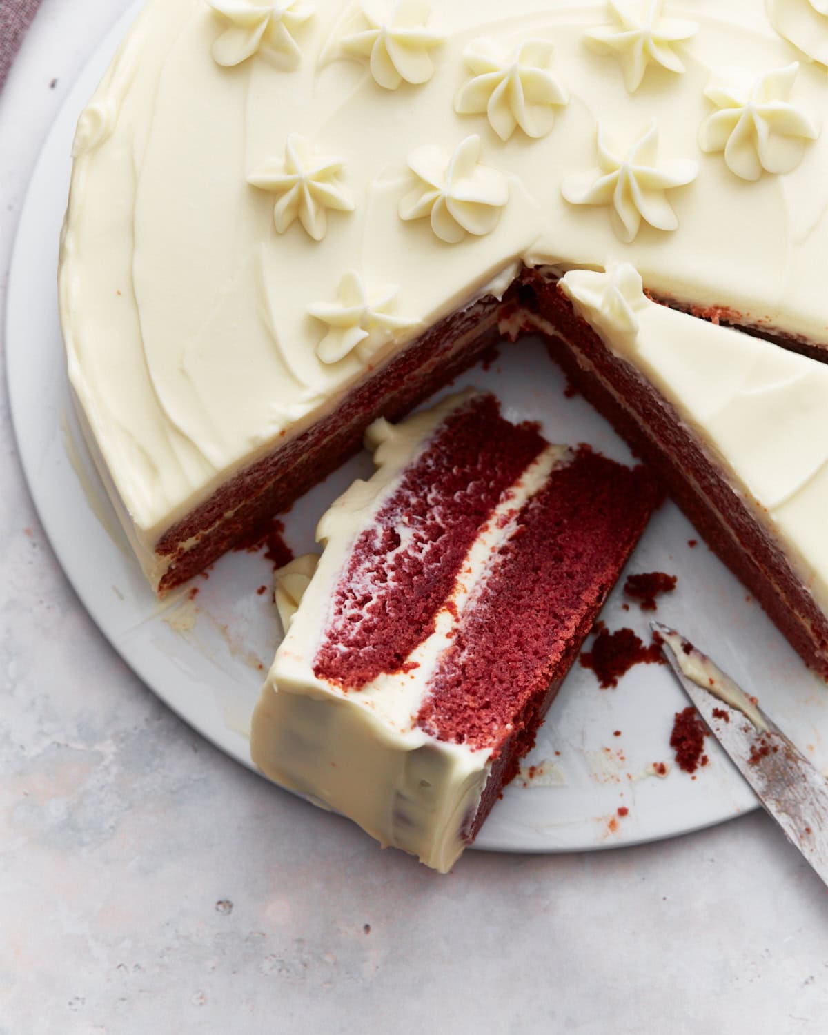 Gluten-free red velvet cake with cream cheese frosting, decorated with piped flowers, and a slice partially removed